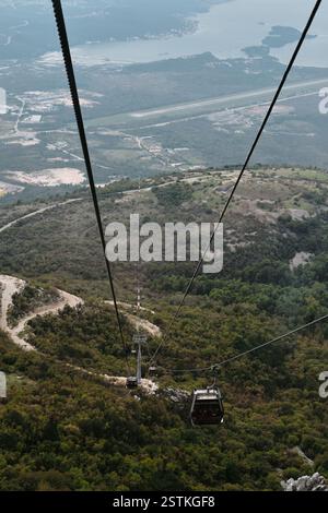 Ein Blick aus der Höhe auf die Seilbahn, die über üppige grüne Hügel hinabsteigt, bietet eine atemberaubende Perspektive auf die Landschaft darunter. Flughafen Tivat Stockfoto