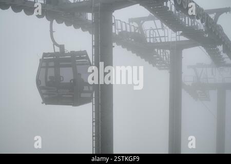 Eine Seilbahn mit der Bezeichnung „Kotor Cable Car“ steigt durch dichten Nebel auf und verschwindet im Nebel. Passagiere sitzen im Inneren, kaum sichtbar. Kotor, Montenegro Stockfoto