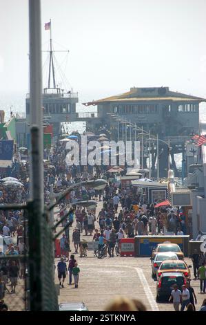 An einem Sommertag voller Menschenmengen am Santa Monica Pier, bei denen die Menschen entlang des geschäftigen Piers spazieren und die lebhafte Atmosphäre und die Meeresbrise genießen Stockfoto