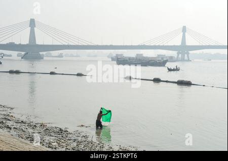 Die Einheimischen waschen ihre Kleidung im Flusswasser, wo sich Plastik- und Müllhaufen auf den Fluss und seine Ufer füllen, was der Meeresökologie und der öffentlichen Gesundheit schadet. Chittagong, Bangladesch. Stockfoto
