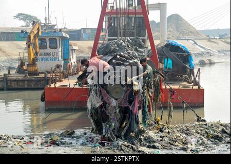 Arbeiter entfernen Kunststoff und andere Ablagerungen aus dem Schleifkopf einer Grabmaschine entlang der verschmutzten Ufer des Karnaphuli River in Chittagong. Müllhaufen haben den Fluss kontaminiert, sich an den Ufern ansammeln und sowohl das Meeresökosystem als auch die menschliche Gesundheit schädigen. Bangladesch. Stockfoto