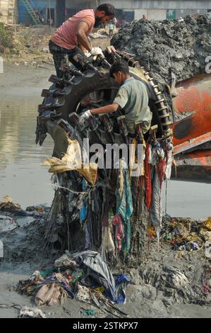 Arbeiter entfernen Kunststoff und andere Ablagerungen aus dem Schleifkopf einer Grabmaschine entlang der verschmutzten Ufer des Karnaphuli River in Chittagong. Müllhaufen haben den Fluss kontaminiert, sich an den Ufern ansammeln und sowohl das Meeresökosystem als auch die menschliche Gesundheit schädigen. Bangladesch. Stockfoto
