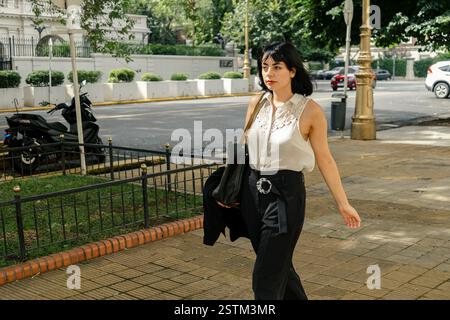 Selbstbewusste hispanische Geschäftsfrau, die auf einem Bürgersteig der Stadt läuft, Tasche und Blazer trägt und urbanen professionellen Stil zeigt Stockfoto