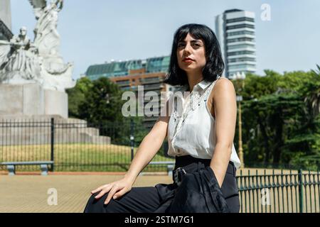 Stilvolle Geschäftsfrau in einem Park in montevideo, uruguay, mit einem historischen Denkmal und modernen Gebäuden im Hintergrund Stockfoto