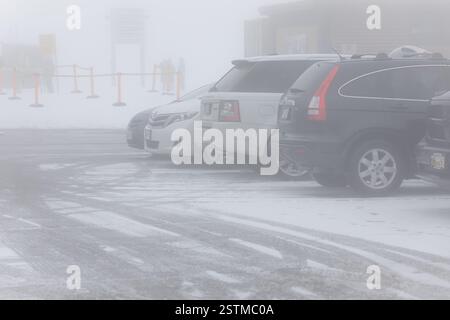 Schlechte Sicht, Autos parken an einem nebeligen Wintertag. Ein nebeliger Wintertag auf dem Parkplatz mit schneebedeckter Straße. Autos parkten auf einer nebeligen Winterstraße Stockfoto