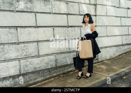 Eine elegante Geschäftsfrau hält eine Einkaufstasche und trägt eine schwarze Jacke und ein weißes Hemd Stockfoto