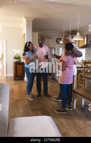 Ältere, vielseitige Freunde feiern zu Hause, lächeln und trinken mit Getränken. Feier, Freundschaft, Zweisamkeit, Party, Entspannung, sammeln Stockfoto