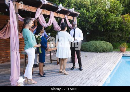 Seniorenpaare, die am Pool gelobt werden, umgeben von älteren Freunden und Blumen. Hochzeit, Feier, Zeremonie, Romantik, Commitme Stockfoto