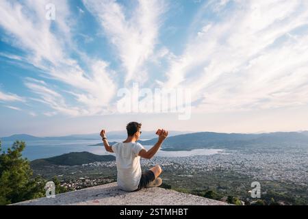 Der Kerl sitzt auf der Kante des Daches, im Hintergrund ist die Küstenstadt. Stockfoto