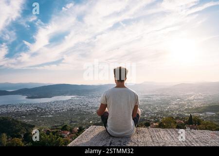 Der Kerl sitzt auf der Kante des Daches, im Hintergrund ist die Küstenstadt. Stockfoto