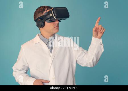 Männlicher Arzt mit einer Virtual-Reality-Brille auf blauem Hintergrund. Ein Arzt in einem VR-Helm auf blauem Hintergrund. Telemedizin-Konzept Stockfoto