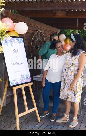 Anlässlich des 60. Geburtstags lächeln zwei verschiedene weibliche Seniorinnen und genießen gemeinsam eine Outdoor-Party. Feier, Freundschaft, Glück, Stockfoto