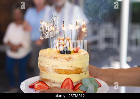 Wir feiern den 60. Geburtstag mit Wunderkerzen auf Kuchen, umgeben von verschiedenen Seniorenfreunden und verschiedenen Seniorenfreunden. Feier, Meilenstein, Party, happ Stockfoto