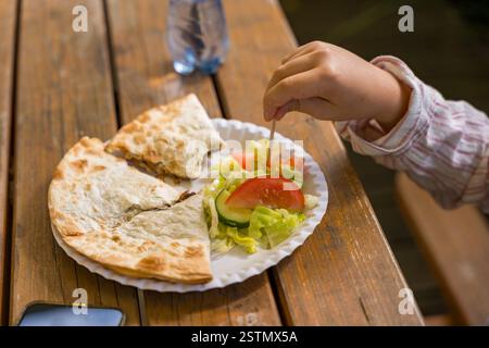 Childs pflücken von Hand Salat von einem Teller mit Quesadilla auf einem rustikalen Holztisch Stockfoto