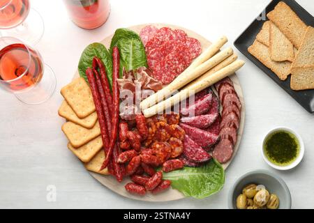 Verschiedene Räucherwürste und andere Snacks serviert mit Wein auf weißem Tisch, flach gelegen Stockfoto