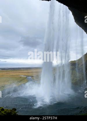 Das Bild zeigt einen atemberaubenden Wasserfall, der von einem felsigen Überhang herabstürzt, umgeben von üppigem Grün und einer weiten Wiese von Grasland Stockfoto