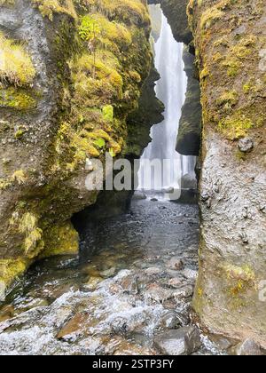 Das Bild zeigt einen atemberaubenden Wasserfall, der durch eine enge Felsschlucht fällt, eingerahmt von hoch aufragenden, mit Moos bedeckten Felsformationen Stockfoto