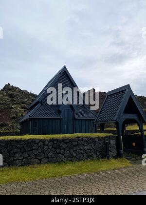Das Bild zeigt ein markantes schwarzes Holzgebäude, das einer traditionellen Kirche ähnelt, auf rauem vulkanischem Felsen, umgeben von üppigem grünem Gras Stockfoto