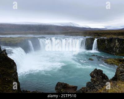 Das Bild zeigt einen atemberaubenden Wasserfall, wahrscheinlich in Island, bekannt als Godafoss, der die raue Schönheit der Natur mit mächtigen Kaskaden und rauer Landschaft zeigt Stockfoto