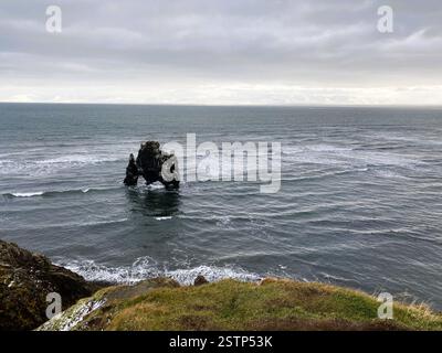 Ein dramatischer Blick auf die Küste mit der Felsformation „Hvitserkur“, umgeben von sanften Wellen und nebeligen Bergen unter grauem Himmel Stockfoto