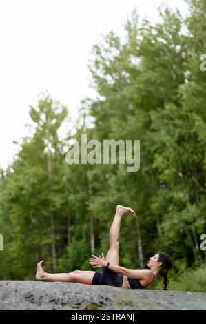 Yoga-Trainer liegt auf rosa Matte, übt Rückenhaltung von Hand bis Großzehe, ein Bein gerade nach oben gestreckt, das andere Bein horizontal gestreckt, tief gestreckt und Stockfoto