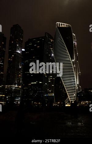 Die Skyline der Stadt mit modernen Wolkenkratzern, die bei Nacht in der Nähe des Ufers in einer belebten städtischen Umgebung beleuchtet werden Stockfoto