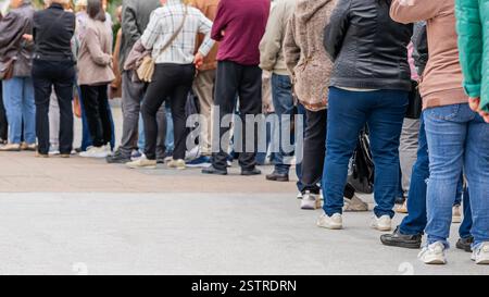 Eine Gruppe anonymer Menschen, die draußen in der Warteschlange stehen, eine lange Reihe von Männern und Frauen, Rückansicht. Das Konzept des Wartens, der Geduld, des urbanen Lebens Stockfoto