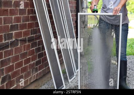 Frau putzt Fensterscheiben mit Wasserschlauch draußen Stockfoto