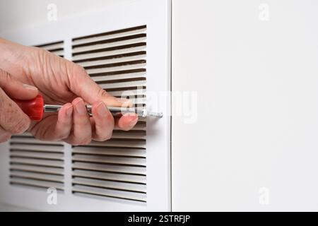 Die Hand des Benutzers verwendet einen Schraubendreher, um die Rückluftdüse für die Reinigung zu öffnen Stockfoto