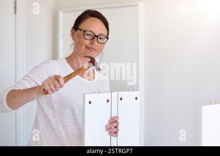 Frau mittleren Alters, die mit einem Hammer Möbel zusammenbaut Stockfoto