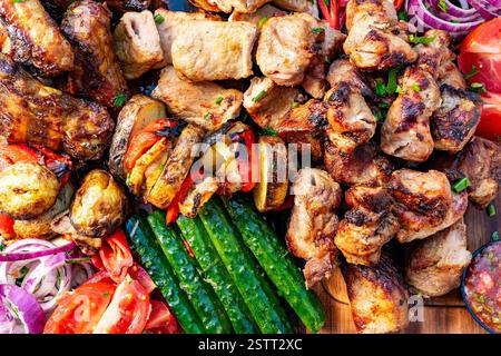 Eine lebendige Platte bietet eine Auswahl an gegrilltem Fleisch und Gemüse, die kunstvoll auf einem Holztisch angeordnet sind. Die farbenfrohe Präsentation zeigt Mundwasser Stockfoto