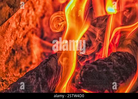 Nahaufnahme von leuchtenden orangen und gelben Flammen mit brennender Glut, die die intensive Hitze und die wirbelnden Rauchmuster in einem Feuer einfangen. Stockfoto