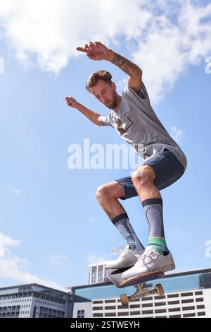 Man, springe und lüfte mit Skateboard für Parkour-Stunt, Extremsport oder coole Fähigkeiten in der Stadt. Männliche Person, Hipster oder Skaten mit Brett, blauer Himmel oder Stockfoto