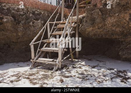 Alte Holztreppe am Strand. Rustikale Leiter in Steinen am tropischen Strand. Alte Treppen auf dem Felsen. Architekturdetails in tropischem Dorf. Stockfoto