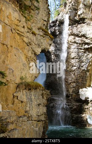Ein atemberaubender Wasserfall stürzt über eine felsige Klippe und erzeugt Nebel und einen klaren türkisfarbenen Pool darunter, umgeben von zerklüftetem Gelände und Nadelbäumen Stockfoto