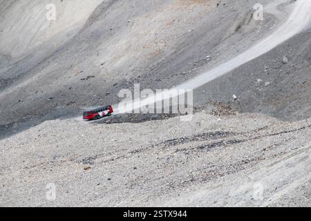 Das Bild zeigt eine zerklüftete, bergige Landschaft mit einem roten Fahrzeug, das auf einer kurvenreichen Feldstraße durch felsiges Gelände fährt und Abenteuer zeigt Stockfoto