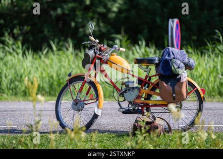 Gelbes und rotes Oldtimer-Moped, Rennrad steht auf der Straße. Ein altes Moped mit Satteltaschen und Gummibändern. Sommerreise auf einem Moped. Stockfoto