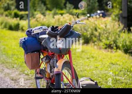 Gelbes und rotes Oldtimer-Moped, Rennrad steht auf der Straße. Ein altes Moped mit Satteltaschen und Gummibändern. Sommerreise auf einem Moped. Stockfoto