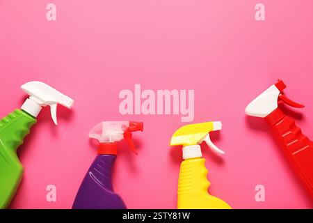 Bunte Sprühflaschen mit Reinigungsprodukten auf rosafarbenem Hintergrund, flache Lagen. Leerzeichen für Text Stockfoto