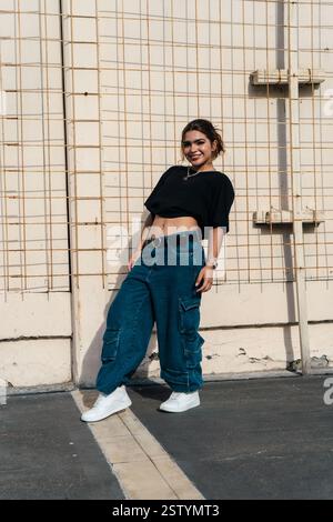 Stilvolle Frau posiert selbstbewusst draußen vor einer strukturierten Wand Stockfoto