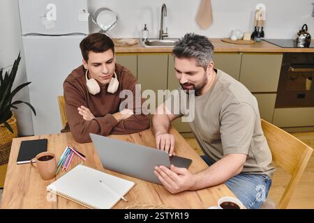 Zwei Brüder sitzen zusammen an einem Holztisch und nehmen an einer gemeinsamen Aktivität mit einem Laptop Teil. Stockfoto
