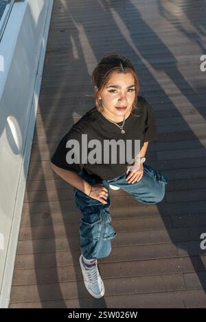Porträt einer stilvollen jungen Frau, die sich auf einem modernen Holzsteg hockt Stockfoto