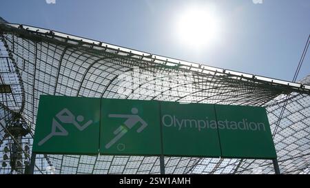 Foliendachkonstruktion des Olympiastadions in München mit dem berühmten Olympiastadion-Schild im Vordergrund unter blauem Himmel mit Sonnenschein Stockfoto