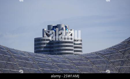 Foliendachkonstruktion des Olympiastadions in München mit dem berühmten BMW Hochhaus im Hintergrund unter blauem Himmel bei Sonnenschein Stockfoto