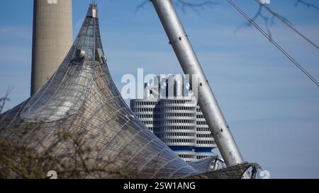Foliendachkonstruktion des Olympiastadions in München mit dem berühmten BMW Hochhaus im Hintergrund unter blauem Himmel bei Sonnenschein Stockfoto