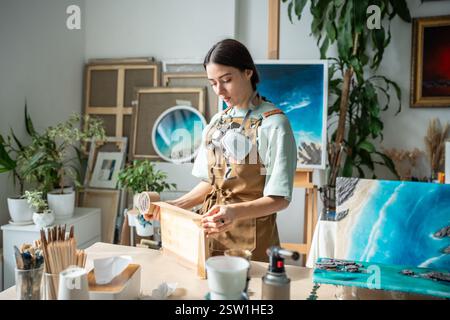 Zielgerichtete Frau organisiert den Arbeitsplatz, bereitet Werkzeuge, Verbrauchsmaterialien und Arbeitsflächen für kreative Prozesse vor. Stockfoto