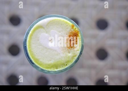 Ein schaumiges grünes Getränk mit herzförmigem Design und einem Spritzer Gewürz Stockfoto