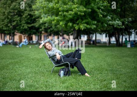 Entspannte Frau beim Nickerchen, auf Klappstuhl auf dem Rasen im Naturpark draußen Stockfoto