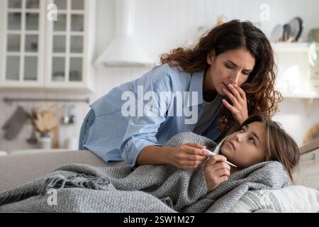 Besorgte Mutter, die Thermometer ansieht und die Temperatur der kranken Tochter im Bett prüft Stockfoto