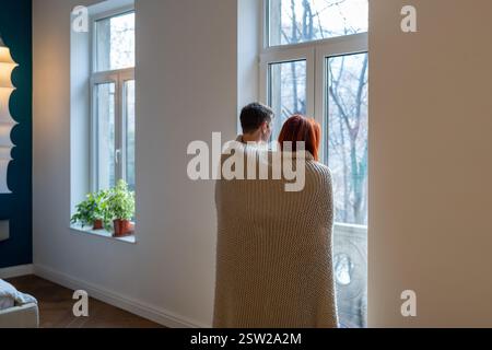 Ein Paar, in eine Decke gewickelt, mit Blick aus dem Fenster Stockfoto
